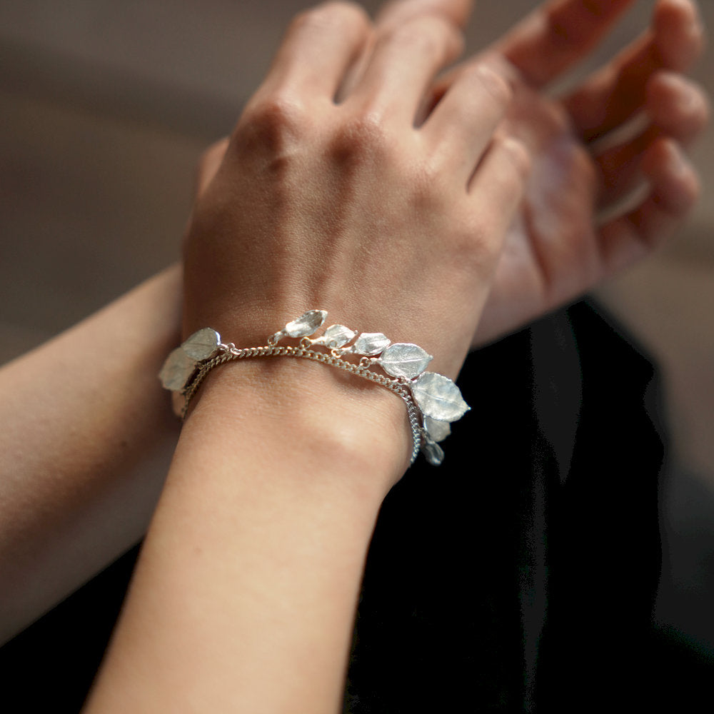 Close-up of a hand wearing a designer bracelet with unique leave charms
