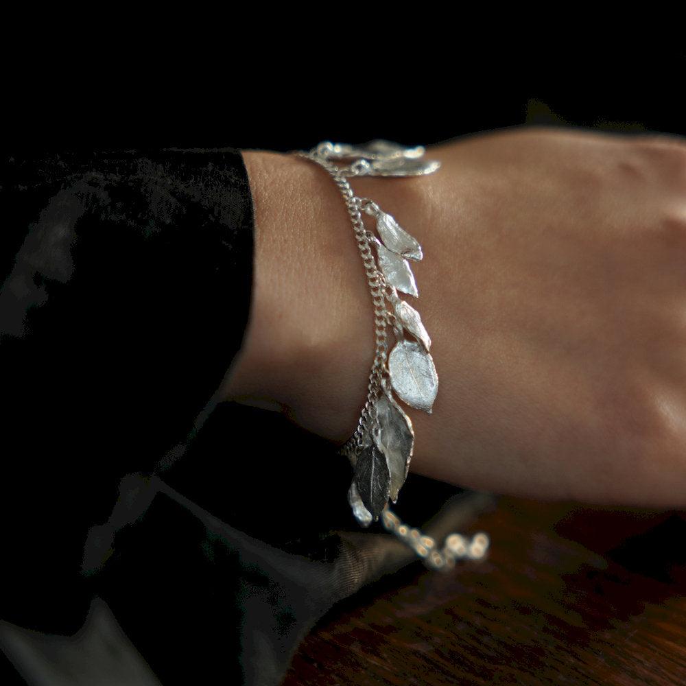 Silver botanical bracelet with leaf-shaped charms on a wrist