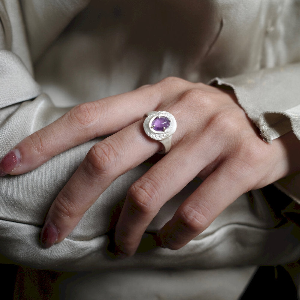 Hand wearing a handcrafted silver ring with an amethyst stone on a neutral background