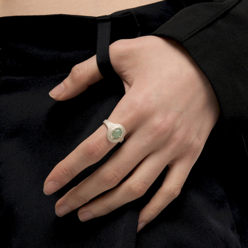 Hand wearing a ring with a green gemstone on a black background