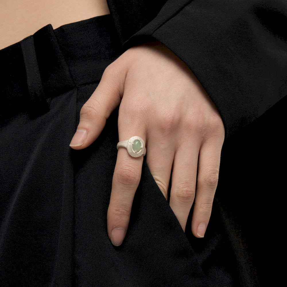 Hand wearing a handmade ring with a green gemstone against a black background