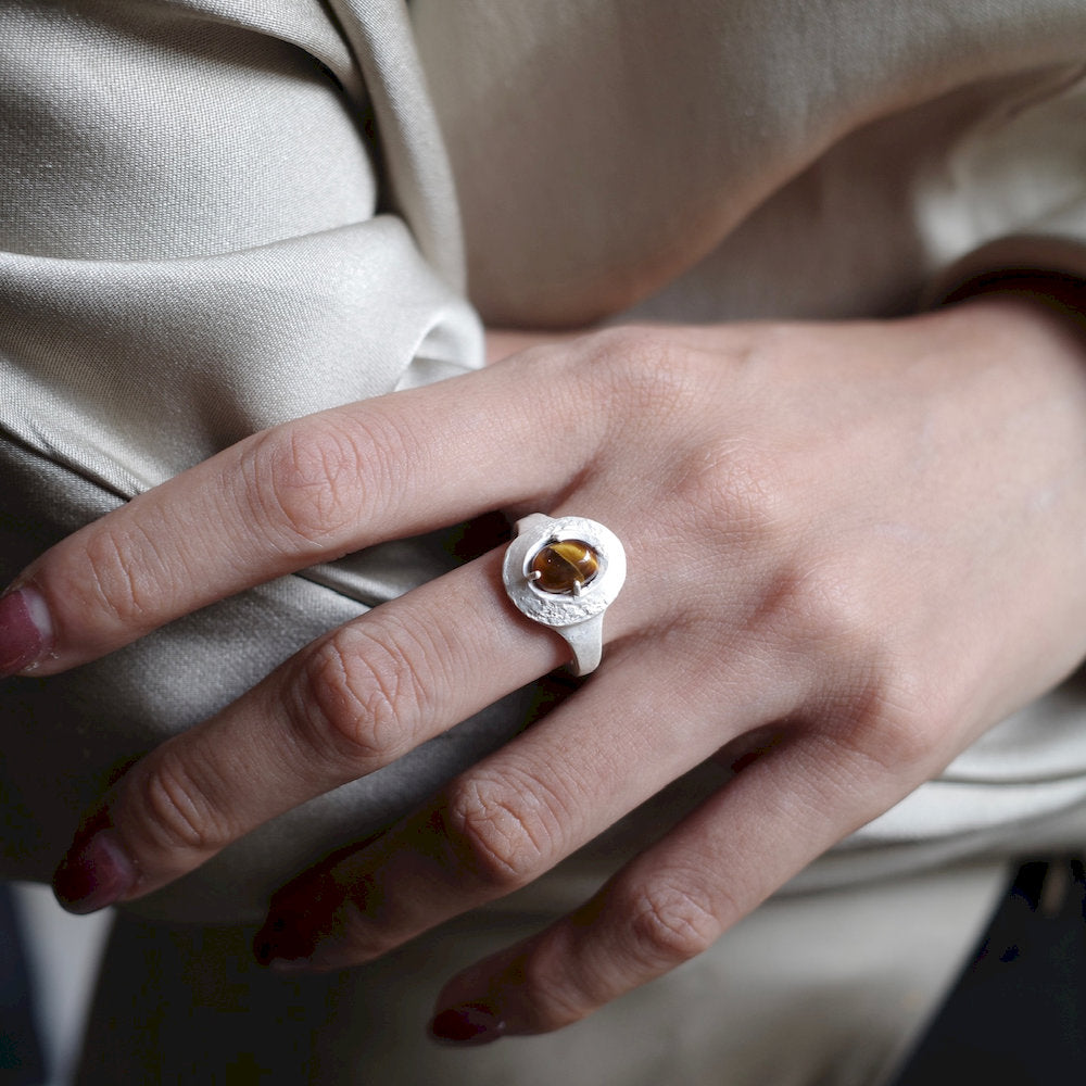 Close-up of a hand wearing a Sacral Ring with a brown gemstone against a neutral background