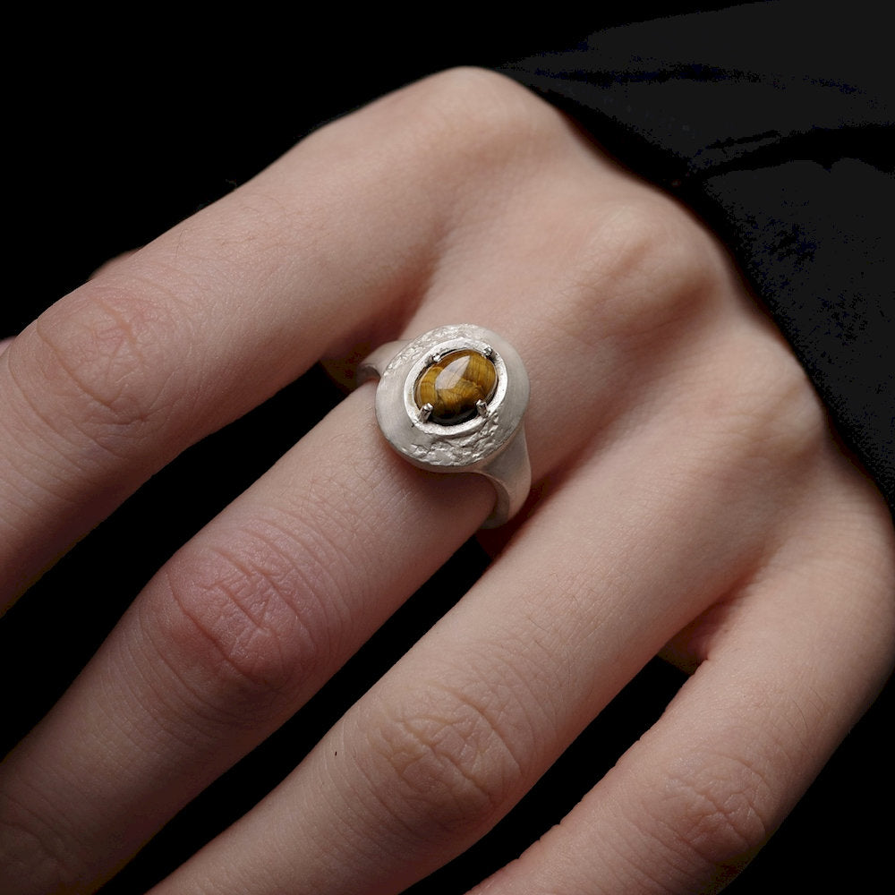 Silver ring with a brown gemstone on a person's finger against a black background
