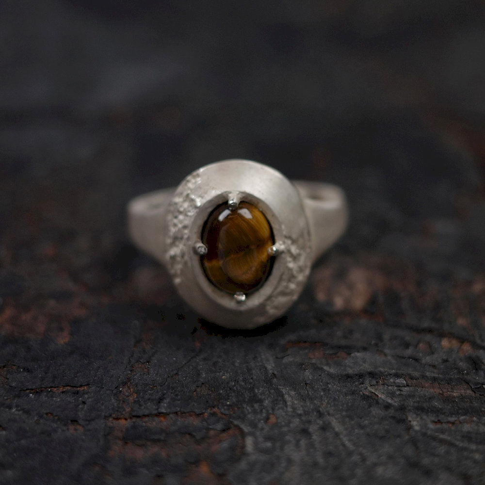 Handcrafted silver ring with a brown gemstone on a dark textured surface