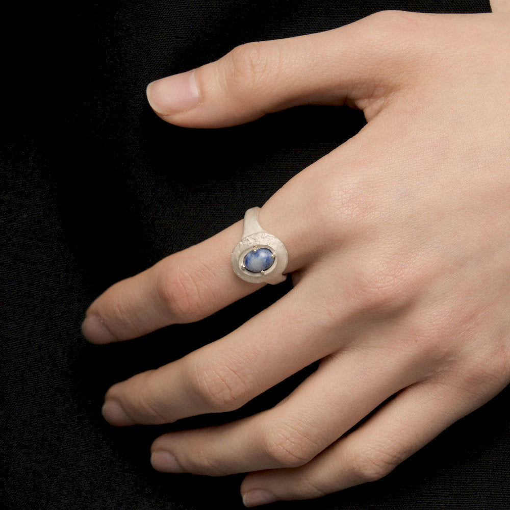 Hand wearing a Throat Ring with a blue gemstone on a black background