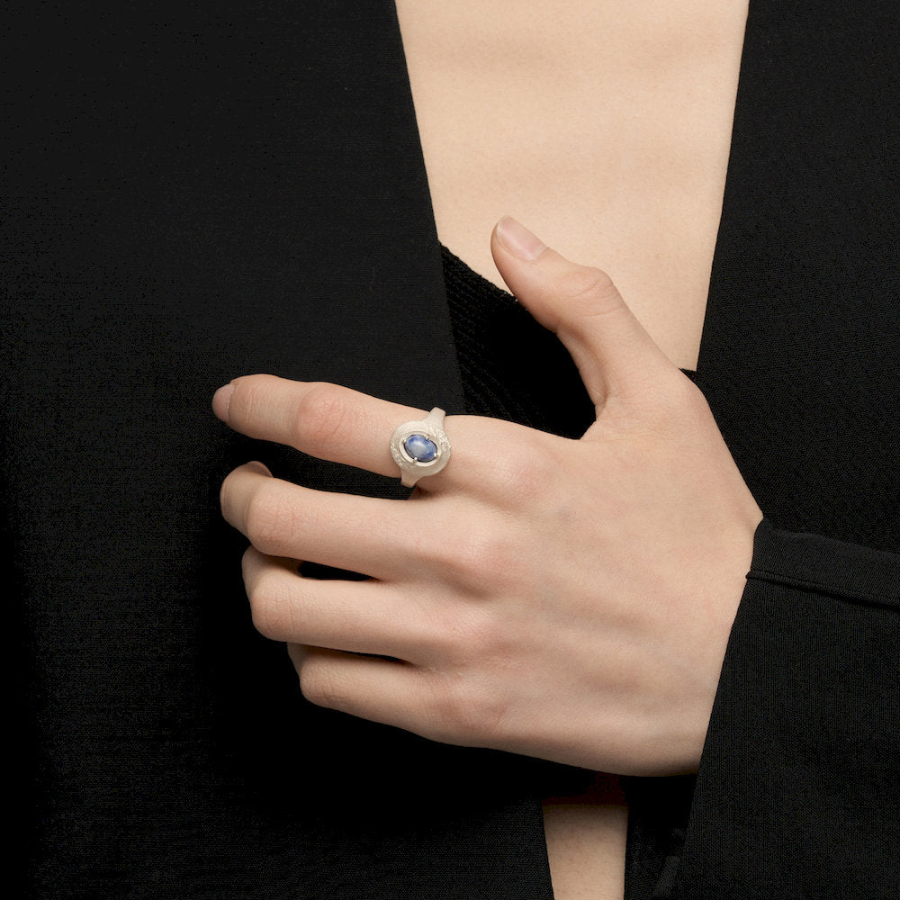 Hand wearing a ring with a blue gemstone against a black background