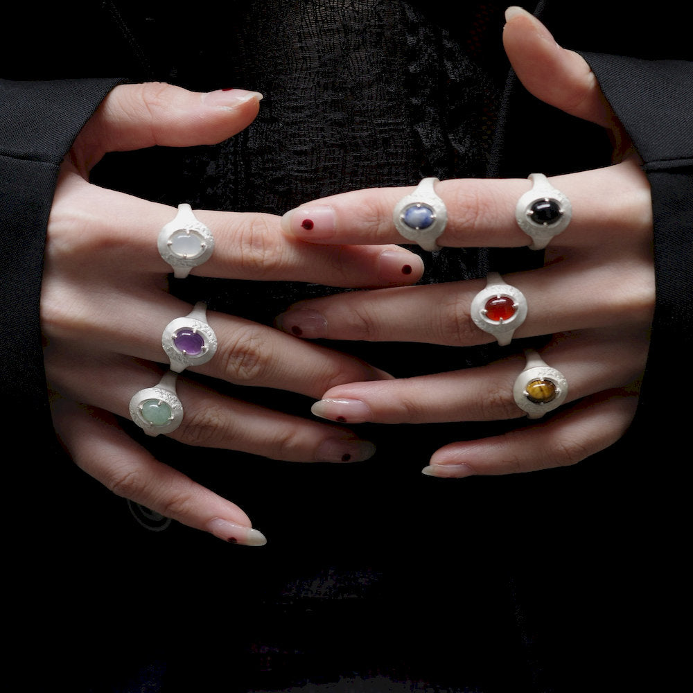 Hands wearing multiple energy rings with colorful gemstones against a black background