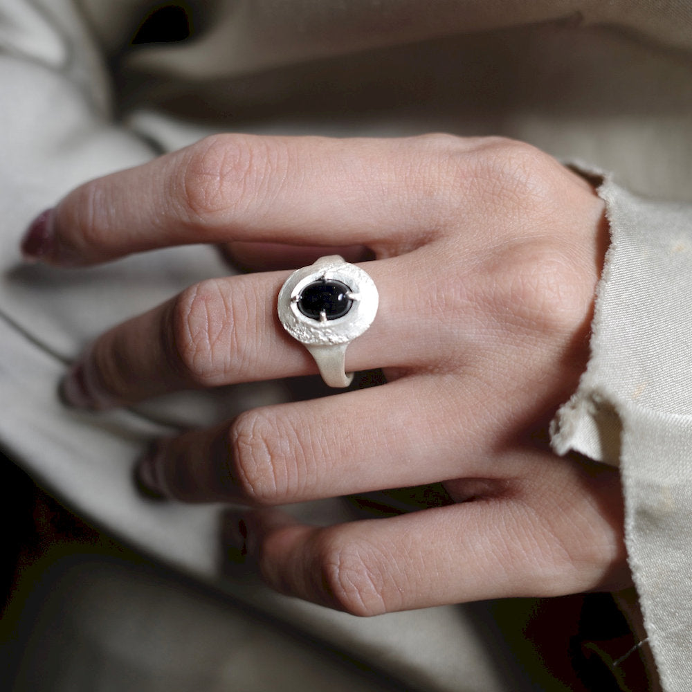 Close-up of a hand wearing a Root Ring with a black gemstone.