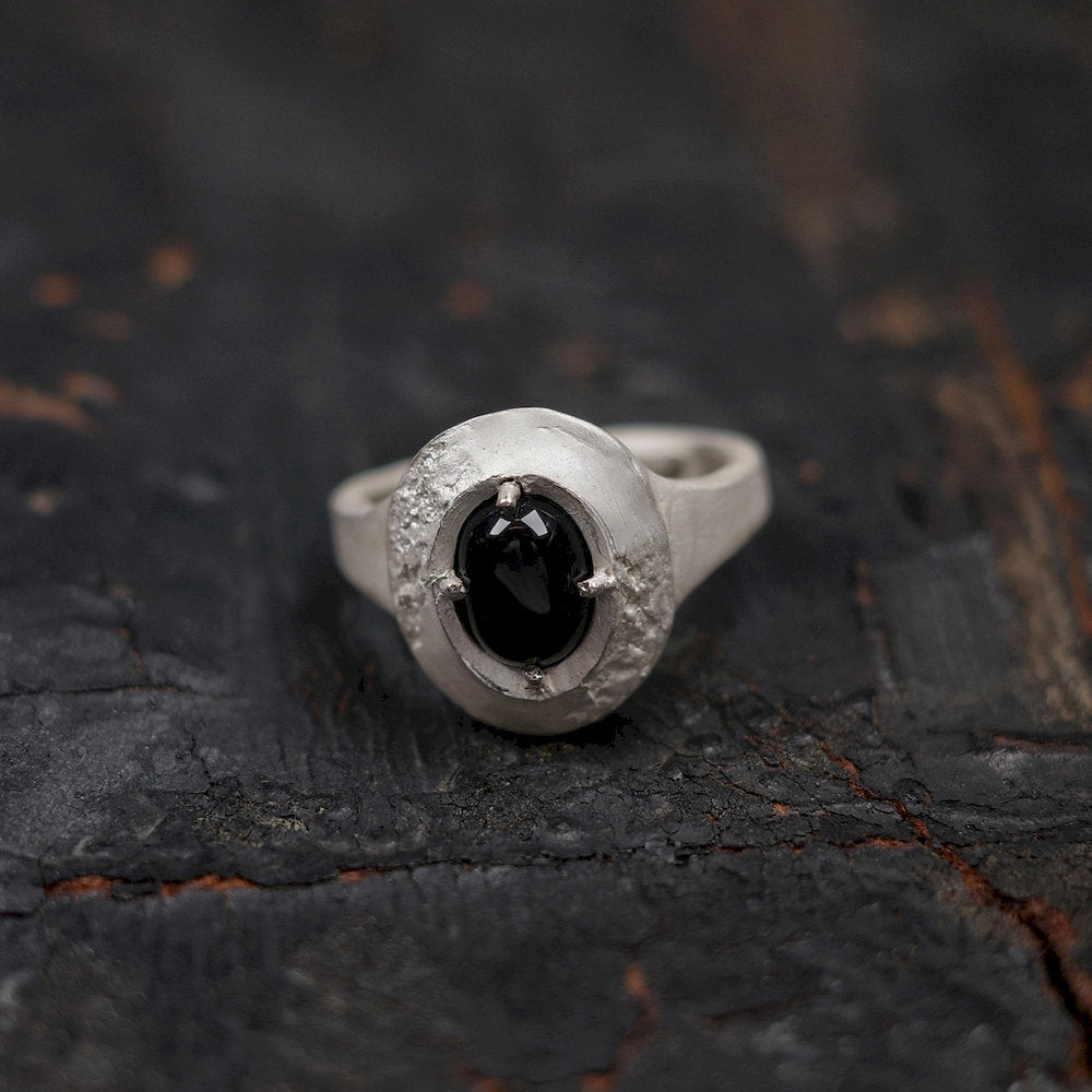 Silver ring with a black gemstone on a textured dark surface
