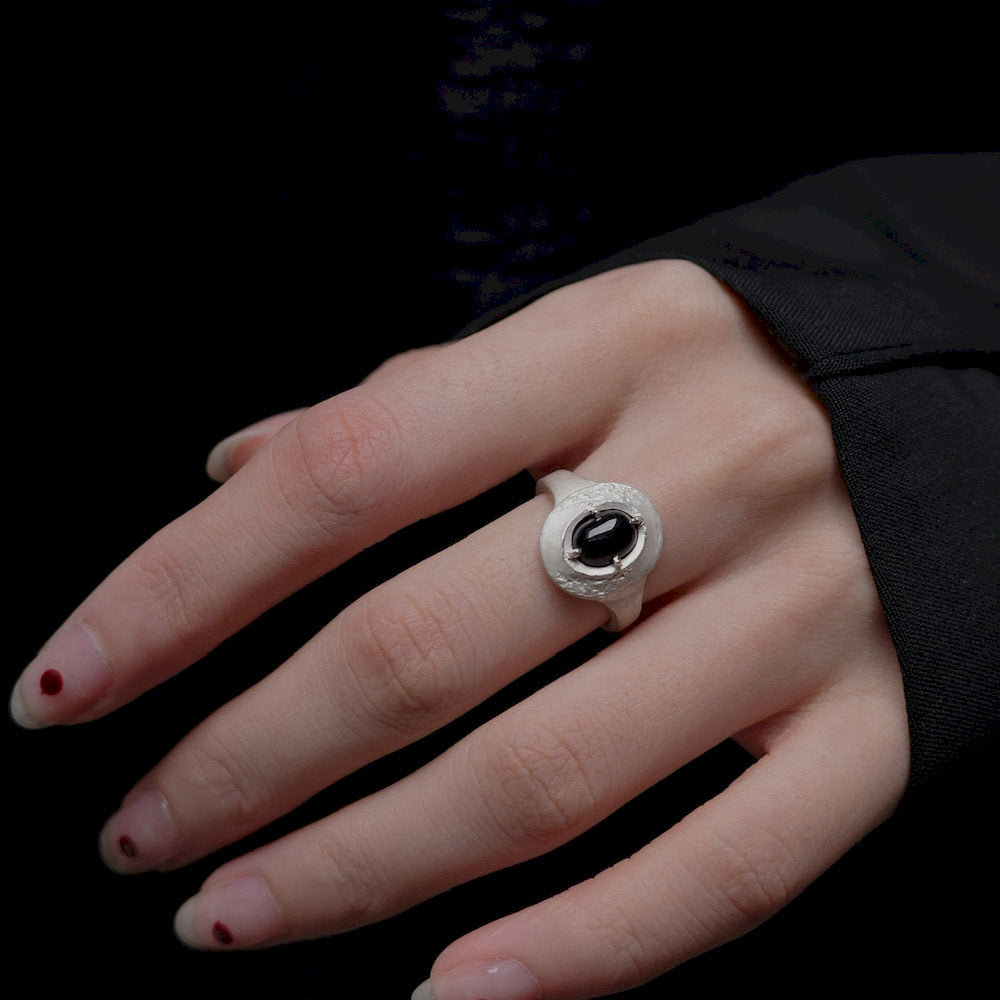 Hand wearing a silver ring with a black gemstone on a dark background