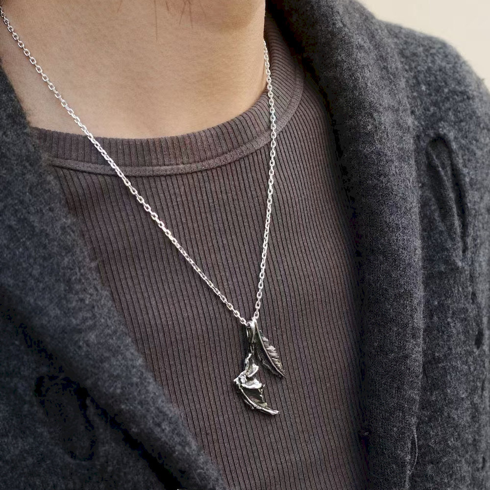 Person wearing a dark silver necklace with a handcrafted fantasy pendant on a plain background