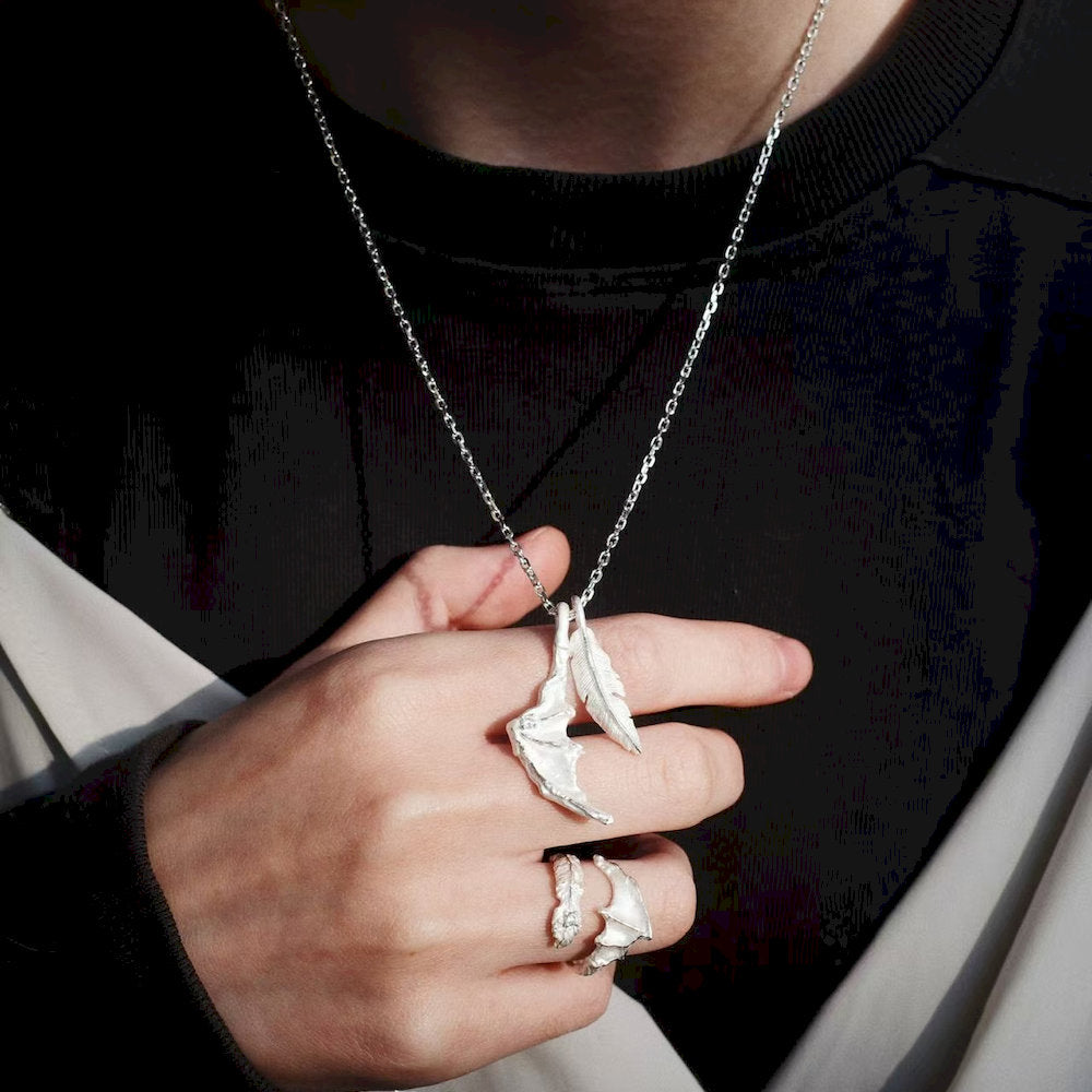 Person wearing a silver dragon wing set of a necklace and a ring on a dark background