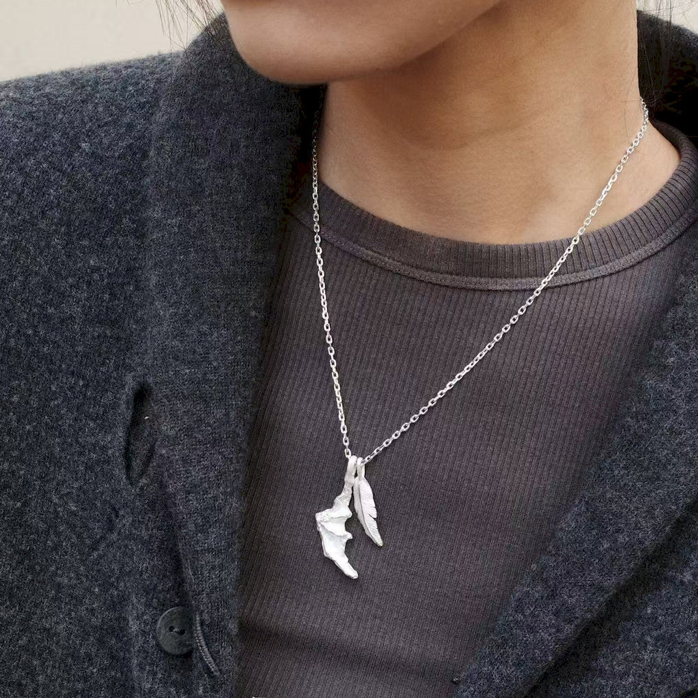 Person wearing a silver necklace with a unique dragon wing pendant