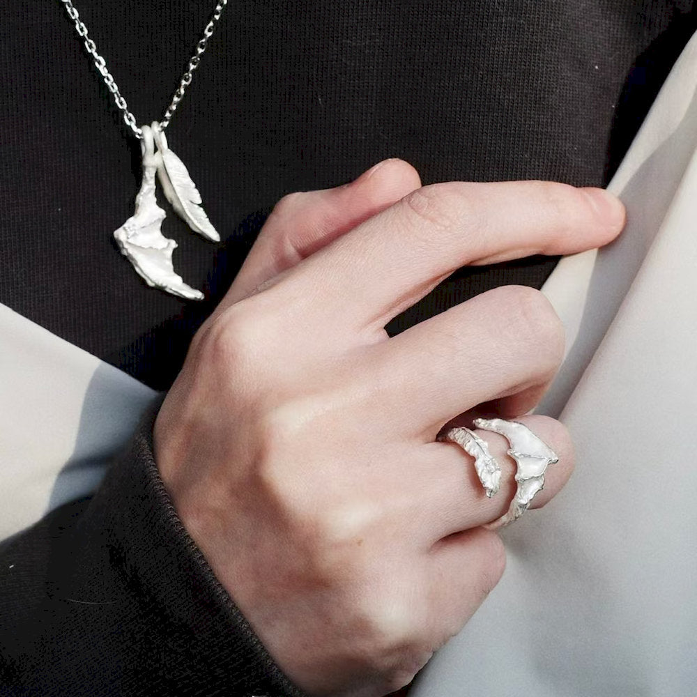 Hand wearing a sculptural silver ring with a matching necklace