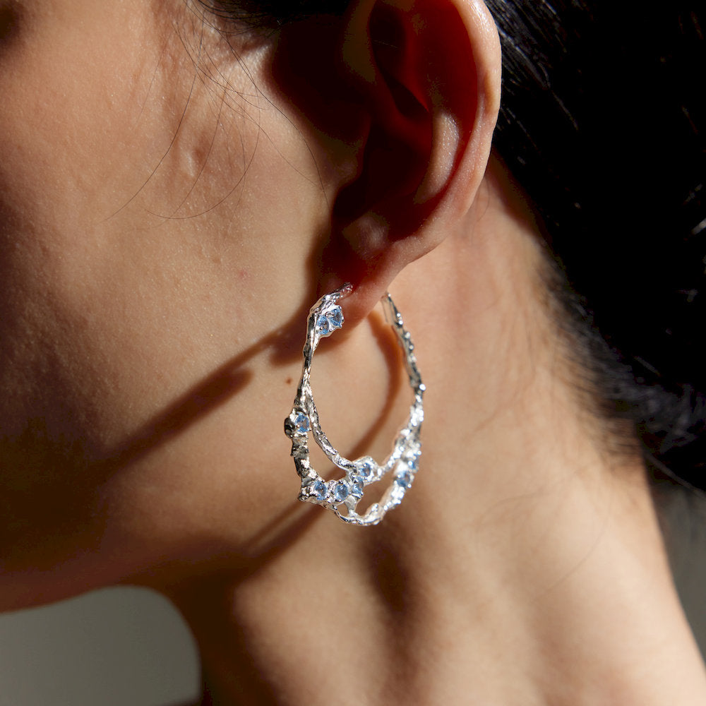 handmade Silver hoop earrings with small sky blue stones worn by a person.