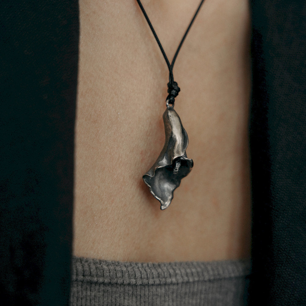 dark Silver flower-shaped pendant on a black cord worn around the neck.